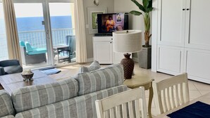 Een moderne woonkamer met een bank, eettafel en een televisie. Er is een balkon met uitzicht op de oceaan.
