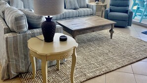 Een woonkamer met een bank, een bijzettafeltje, een lamp en uitzicht op de oceaan door grote ramen.