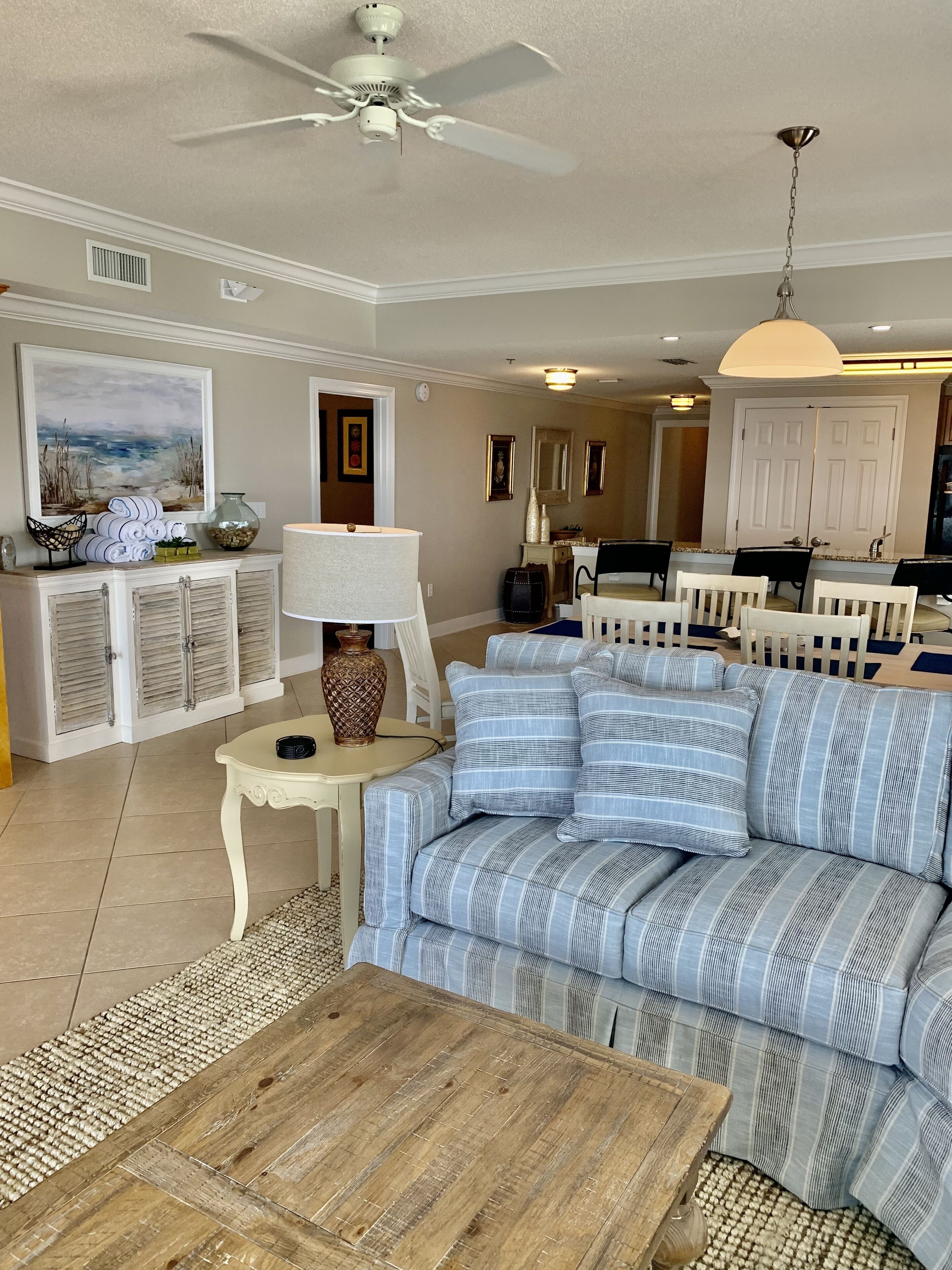 Een woonkamer met een gestreepte bank, een houten salontafel, een plafondventilator en een eethoek met stoelen en een tafel.