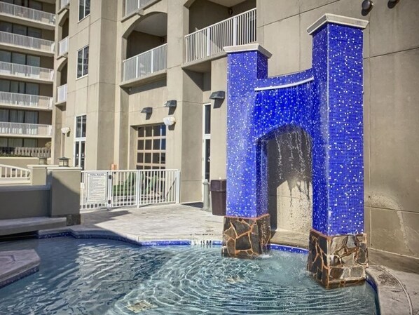 A swimming pool with a blue mosaic archway, surrounded by a building with balconies and a gated entrance. - 1401 (NEW Purchase), East Wrap Ard. View, 2br, Slps8 (Reviews at vrbo.com/511877 (Orange Beach)