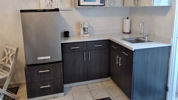 A compact kitchen with dark cabinets, a built-in microwave, a coffee maker, and a sink. - The Charming Unit (5 minutes from Airport) (Carolina)