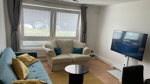Una sala de estar con un sofá, una mesa de centro, un televisor y un ventanal con cortinas.