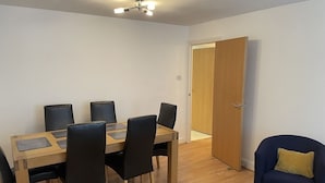 Un comedor con una mesa de madera y sillas negras, un sillón azul, y una puerta que da a otra habitación.