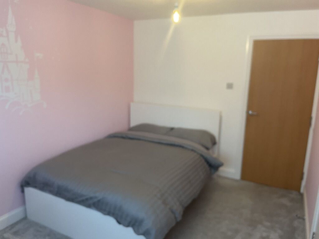 A bedroom with a bed, a door, and a wall with a faint drawing.