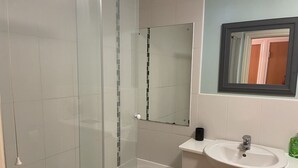 Un baño con cabina de ducha de vidrio, un lavabo blanco y un espejo sobre él.