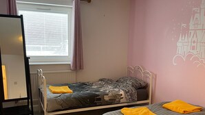 Un dormitorio con dos camas, una ventana con persianas, un radiador, un espejo y una pared con un mural de castillo.