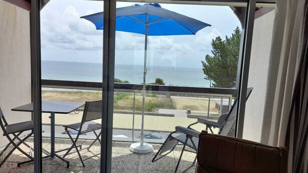 Un balcón con mesa y sillas, una sombrilla azul y vista al mar.