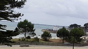 Una playa con arena, árboles y vista al mar con barcos.
