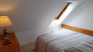 Una habitación pequeña con techo inclinado, una cama individual, una mesita de noche de madera y una lámpara de mesa.