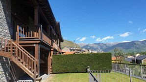 A wooden building with a staircase, a hedge, and a view of mountains.