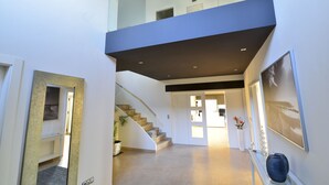 Un intérieur moderne avec un escalier menant à une mezzanine, un couloir doté d’une rambarde en verre et un tableau encadré accroché au mur.