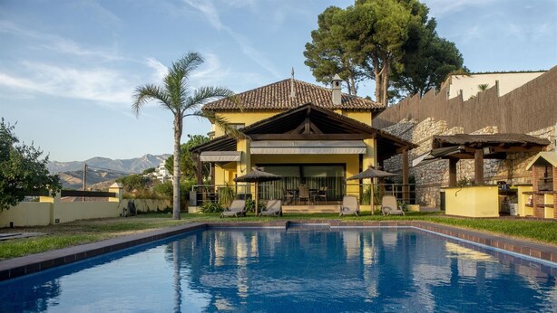 Un espace aménagé au bord de la piscine offrant une vue dégagée sur une maison, une piscine et des montagnes en arrière-plan.