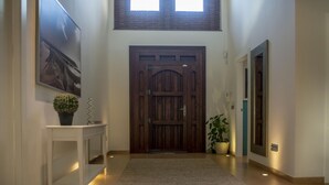 Un couloir avec une porte en bois, une console blanche sur laquelle sont posés un cactus, une plante en pot et un tableau encadré accroché au mur.