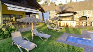 Un espace piscine comprenant des chaises longues, une petite piscine et un bâtiment à la façade en pierre.