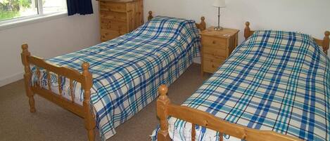 A bedroom with two wooden beds, a wooden dresser, a nightstand, a mirror, and a window with curtains.