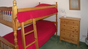 Een stapelbed met een rode matras, een houten dressoir met lades en een spiegel aan de muur.