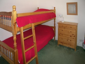 Un lit superposé avec un matelas rouge, une commode en bois avec des tiroirs et un miroir accroché au mur.