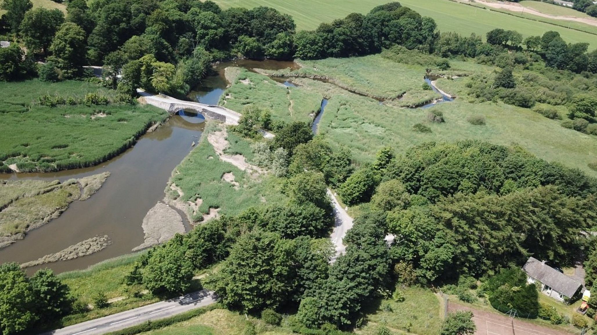 Une vue aérienne d’un paysage rural avec un pont, une rivière et la végétation environnante.