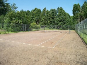 Ein Tennisplatz im Freien mit Netz, umgeben von einem Zaun und Bäumen.