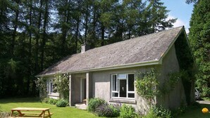 Een gelijkvloers huis met een schuin dak, een veranda en een kleine tuin.