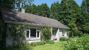 Een gelijkvloers huis met schuin dak, een veranda en een kleine voortuin.