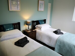 A hotel room with two beds, a nightstand with a lamp, and a window with blinds.