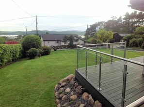 A residential area with a grassy lawn, a wooden deck with a metal railing, and a house in the background.