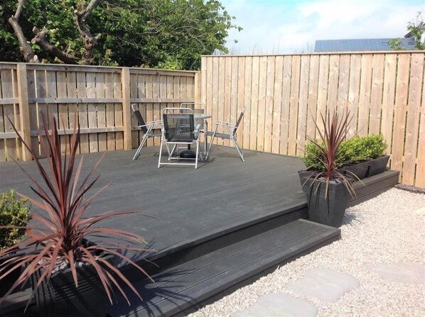 A deck with a table and chairs, surrounded by plants and a wooden fence.