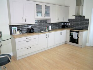 A modern kitchen with white cabinets, a black tiled backsplash, a stainless steel range hood, and a black countertop.