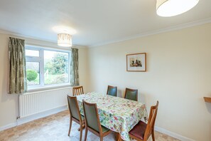 A dining room with a table set for four, a radiator, a window with curtains, and a framed picture on the wall.