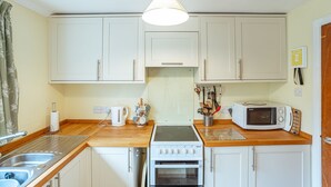 Una cocina compacta con armarios blancos, estufa, microondas y pileta.