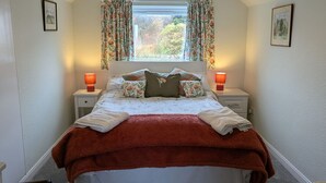 Un dormitorio con cama, dos mesitas de noche, una ventana con cortinas, una lámpara colgante y un cuadro en la pared.