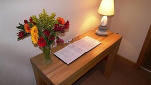 Une table de chevet en bois, sur laquelle se trouvent une lampe allumée, un vase de fleurs et un menu ouvert.