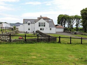 Ein weißes, zweistöckiges Haus mit einer Steinmauer und einem eingezäunten Garten.