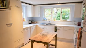 Een keuken met witte kasten, een houten tafel en een raam met uitzicht op groen.