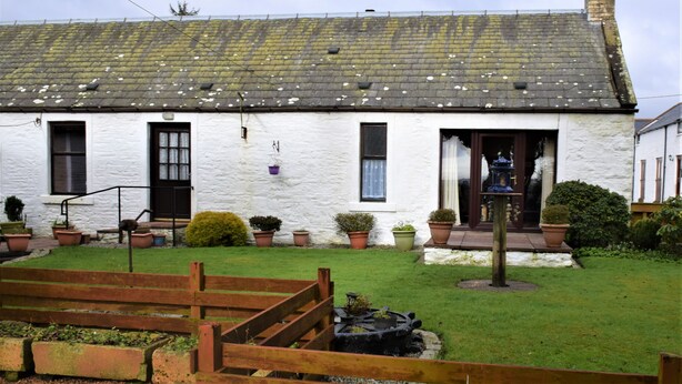 A white building with a tiled roof, multiple windows, and a small garden with potted plants. - Ernambrie Cottage -  a cottage that sleeps 6 guests  in 2 bedrooms (Castle Douglas)