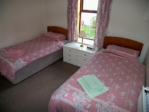 Un dormitorio con dos camas individuales, una mesita de noche con lámpara y una ventana con cortinas.