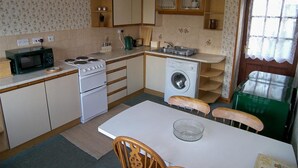 A compact kitchen with a microwave, stove, sink, and washing machine. - Ernambrie Cottage -  a cottage that sleeps 6 guests  in 2 bedrooms (Castle Douglas)