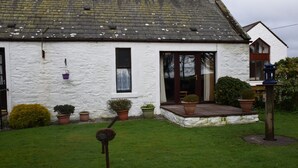 A white house with a sloped roof, a front porch, and potted plants. - Ernambrie Cottage -  a cottage that sleeps 6 guests  in 2 bedrooms (Castle Douglas)