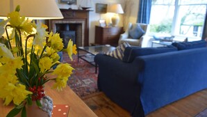 A living room with a blue sofa, a coffee table, and a vase of yellow flowers on a wooden table. - Elm Cottage -  a house that sleeps 8 guests  in 4 bedrooms (Dalbeattie)