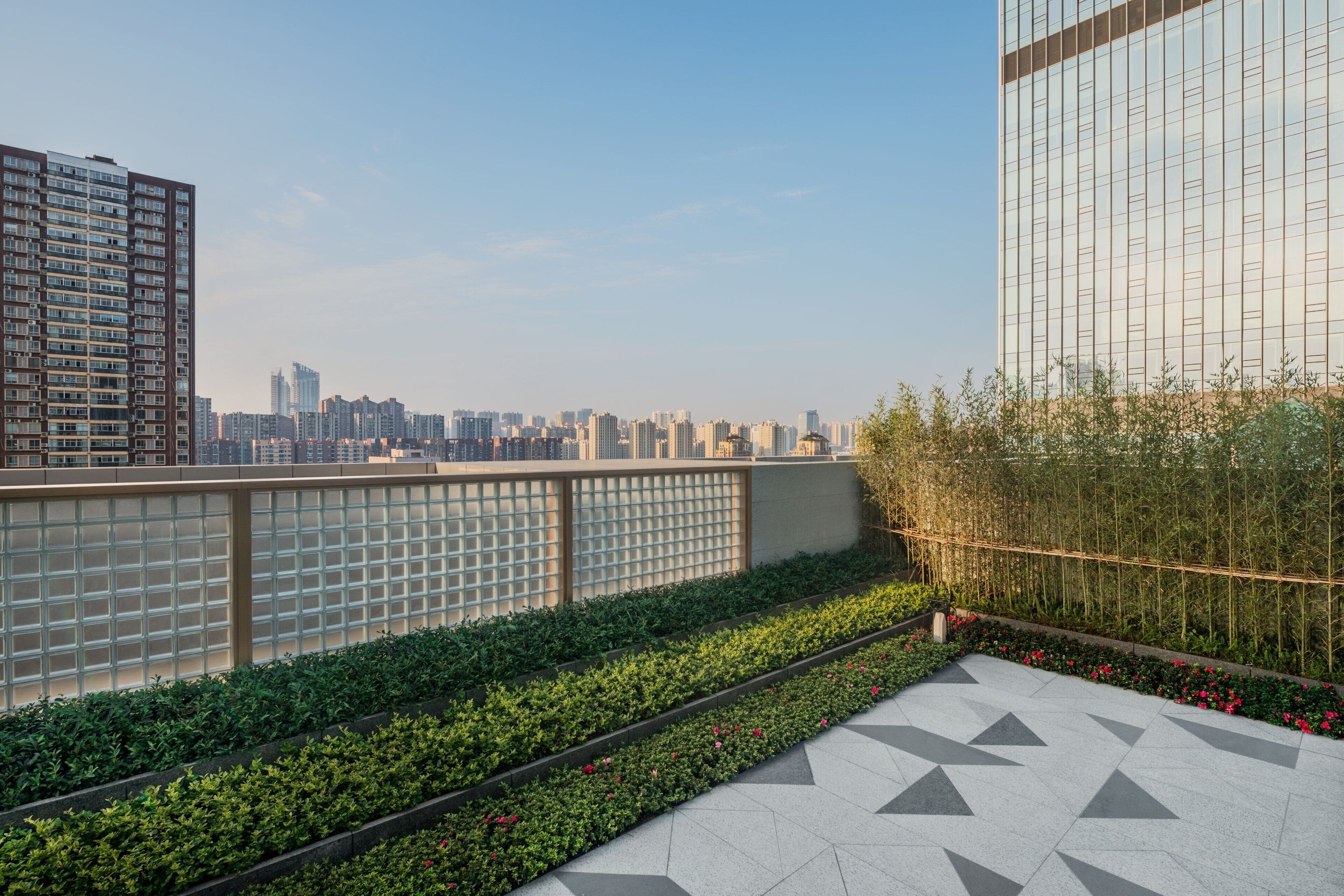A rooftop terrace with a geometric tile floor, a bamboo fence, and a city skyline in the background.
