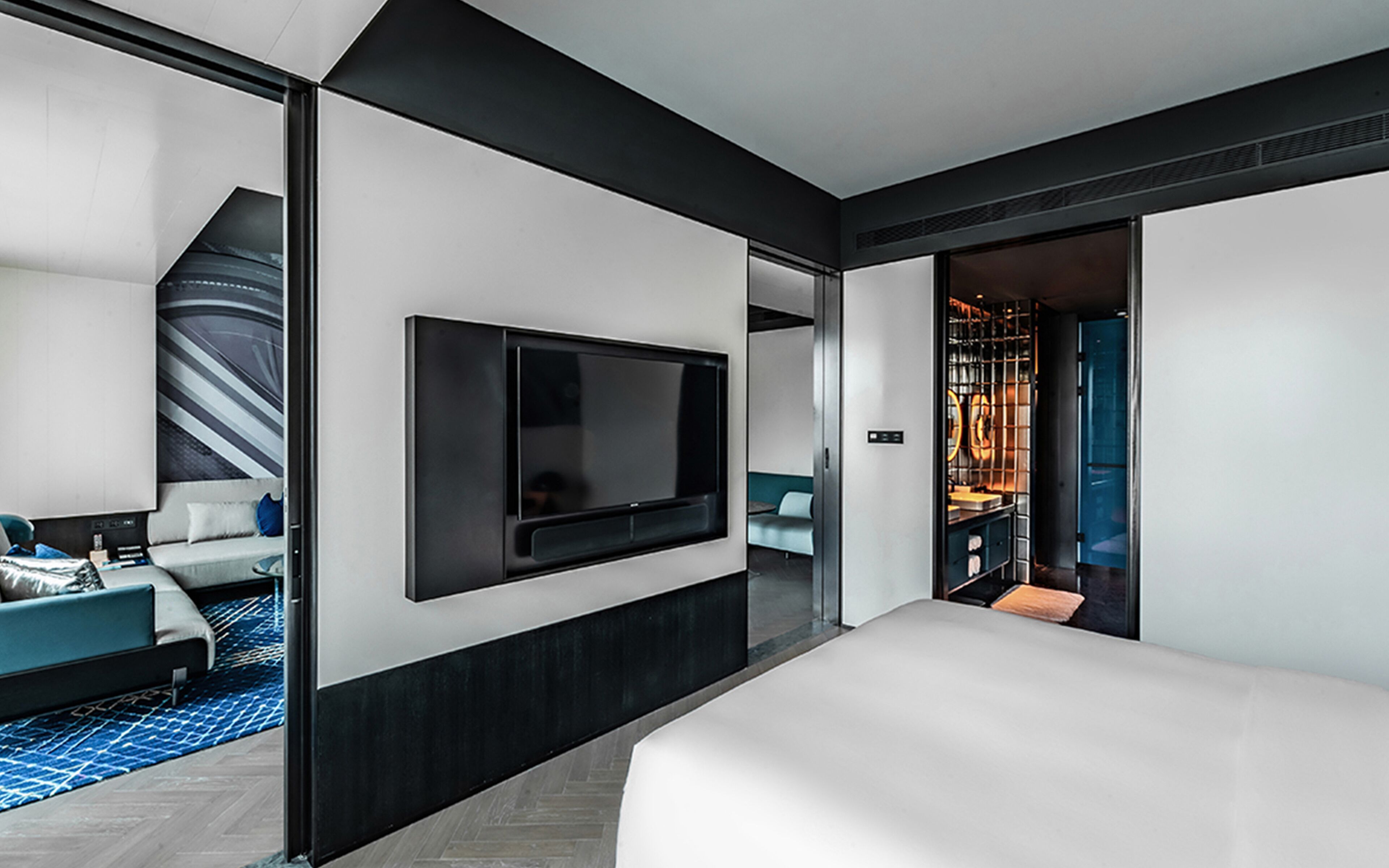 Una habitación de hotel moderna con una cama grande, un televisor de pantalla plana montado en la pared, una zona de estar con sofá y sillas, y vistas al baño.