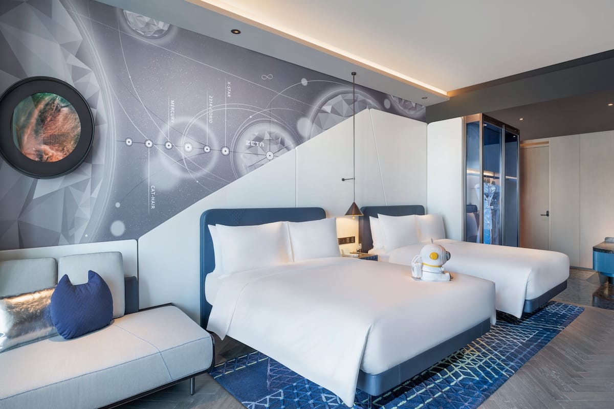 Ein modernes Hotelzimmer mit einem großen Bett, zwei Nachttischen, einem Sofa und einer Wand mit einem Wandgemälde zum Thema Weltraum.