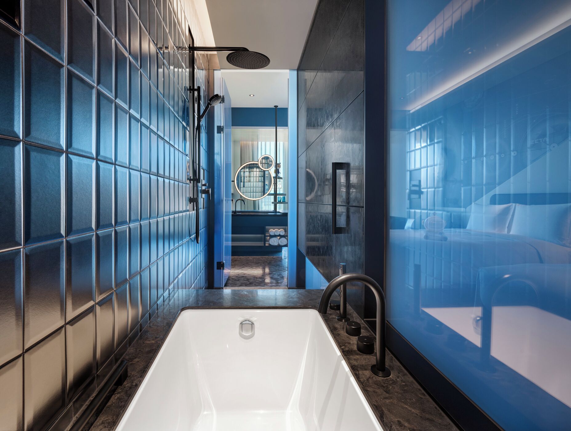 A modern bathroom with a large white bathtub, a glass shower enclosure, and a blue-tiled wall.