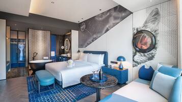 A modern hotel room with a large bed, a sitting area, a bathtub, and a wall with a space-themed mural.