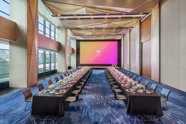 A conference room with a long table, chairs, and a large screen at the front.