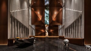 A modern lobby with a central waterfall feature, geometric wall designs, and a reflective floor.