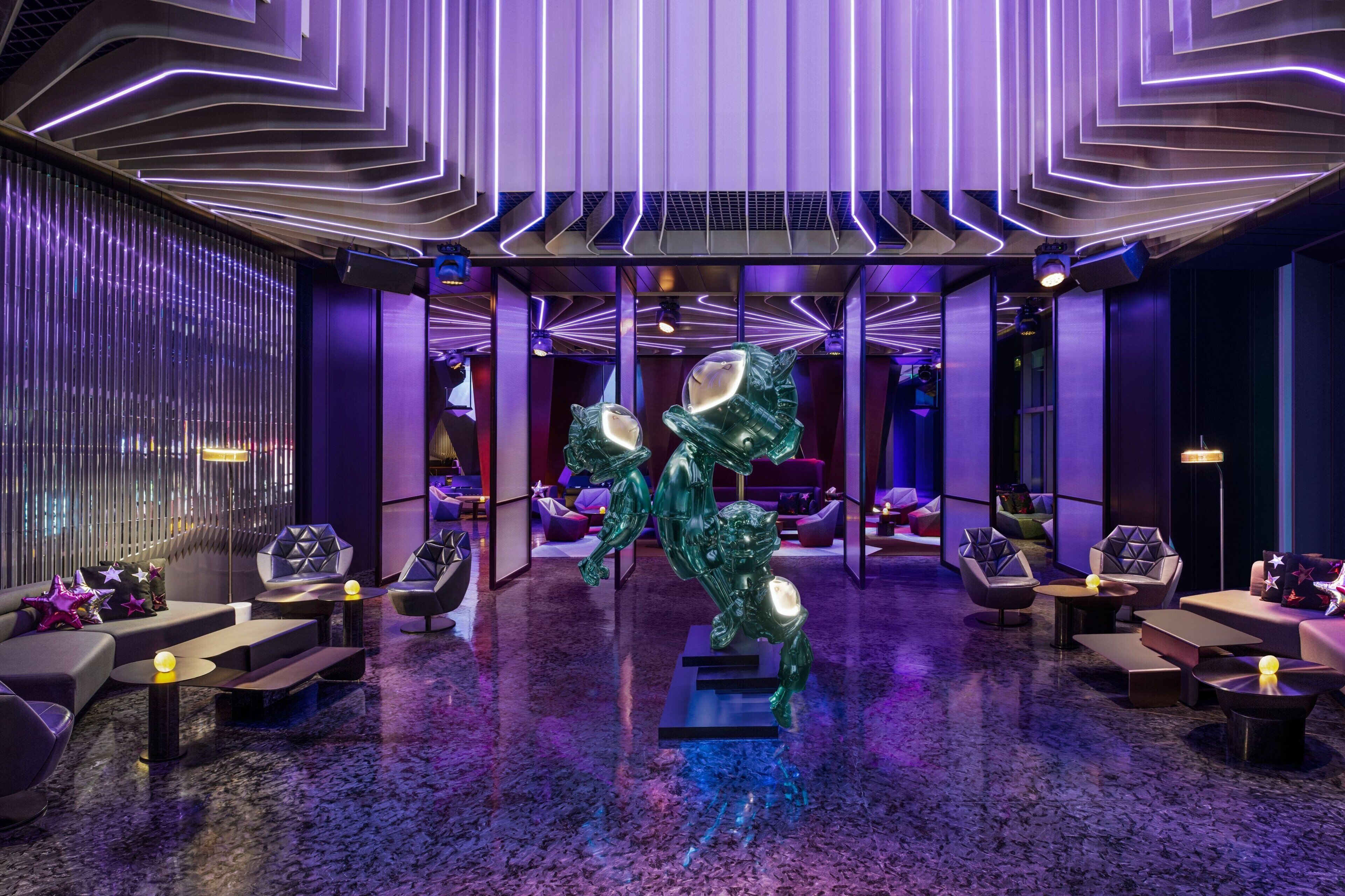 En modern entréhall med en central skulptur, sittgrupper och ett mönstrat tak.