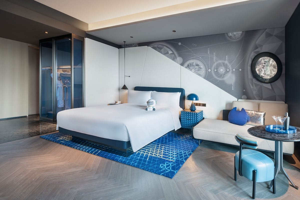 Ein modernes Hotelzimmer mit einem großen Bett, einer Couch, einem kleinen Tisch und einem gläsernen Schrank.