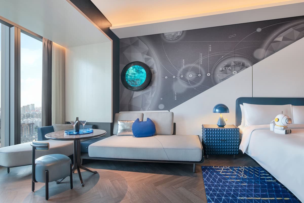Ein modernes Hotelzimmer mit Blick auf die Stadt, einem runden Tisch, einer Couch, einem Bett und einer Wand mit Weltraumdesign.